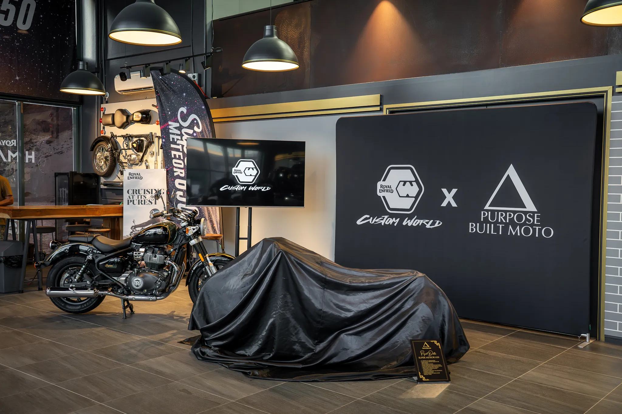 A covered motorcycle on display before its reveal, under industrial pendant lights