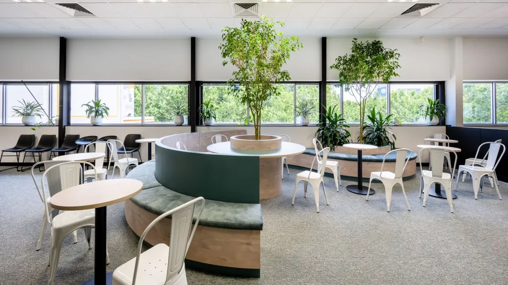 Breakout area with a curved banquette around planting, cafe tables and windows
