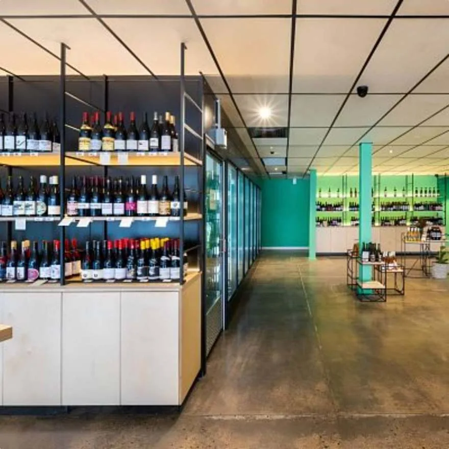 Aisle between green-lit wine shelving and glass-door fridges