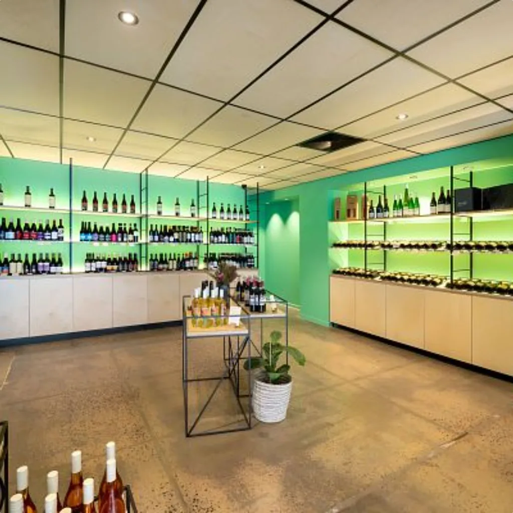 Wine store floor with green-lit timber shelving, glass-door fridges and a central display table