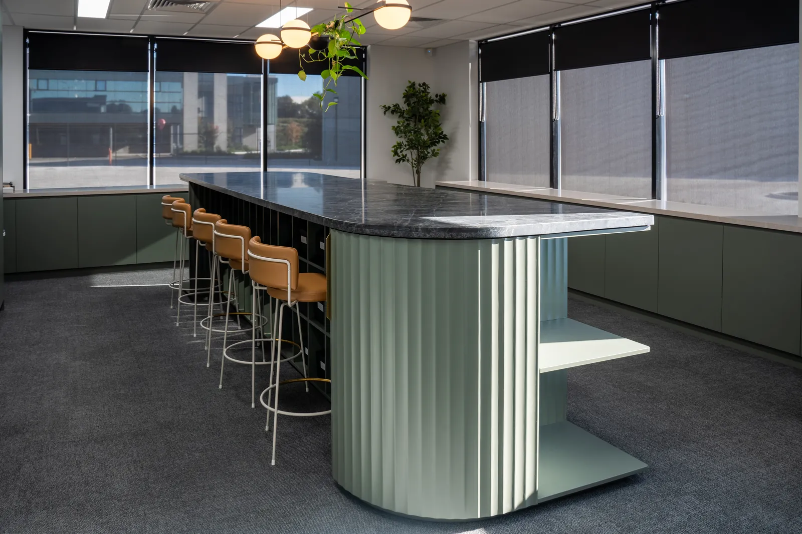 Staff kitchen with a fluted green island, stone top and timber stools