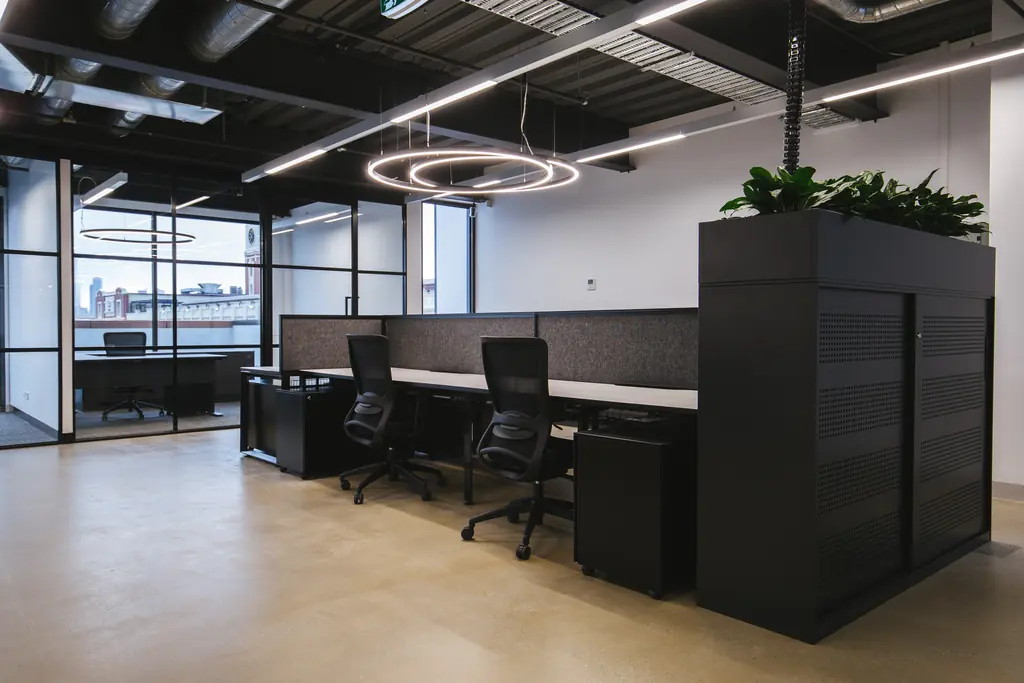 Open-plan workstations with black planter joinery and circular pendant lights, the city skyline beyond